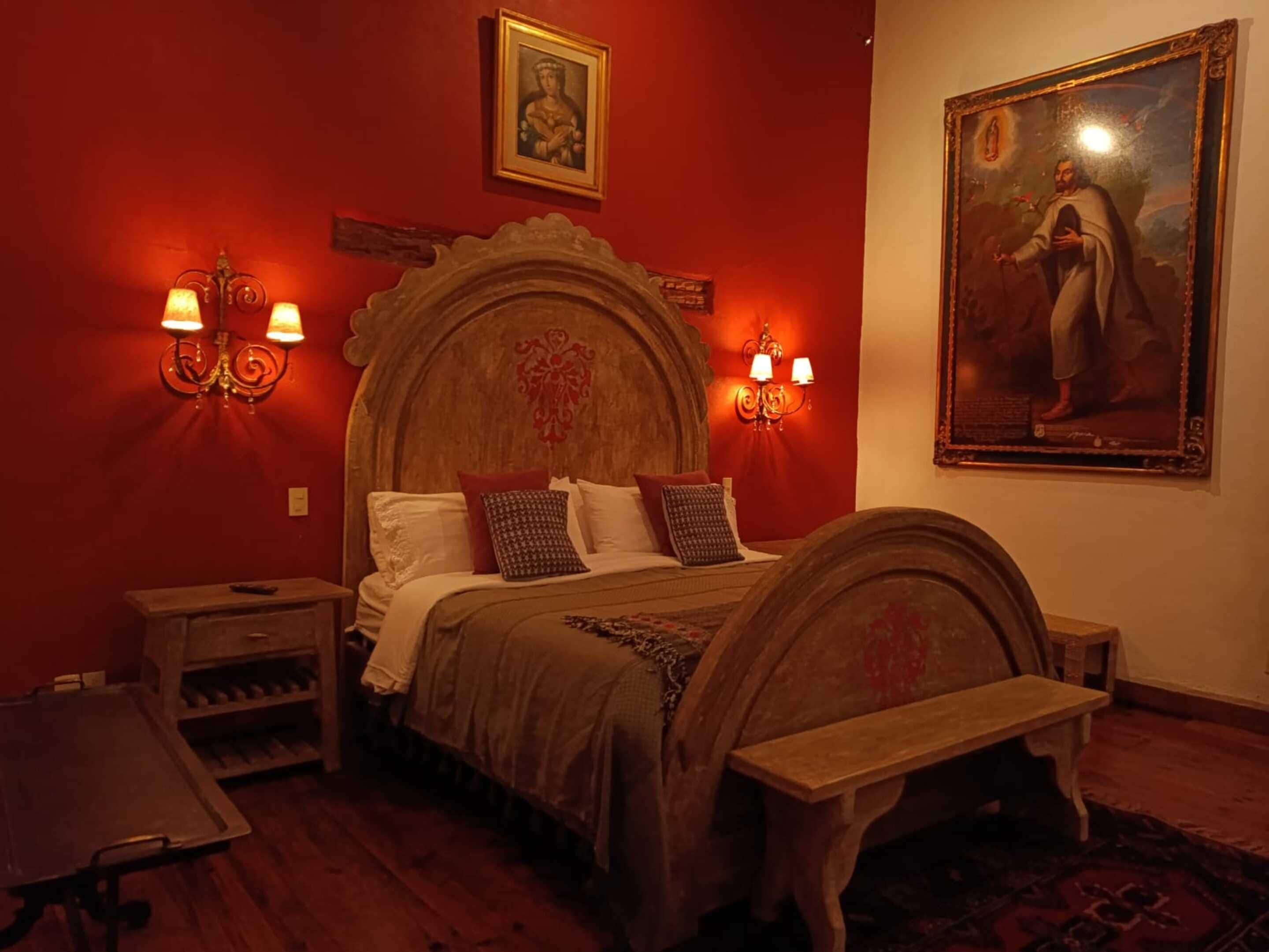 A bedroom with a wooden bed, two bedside tables, a nightstand, a bench, and a painting on the wall.