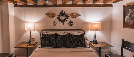 A bedroom with a bed, two bedside tables, a chair, and a ceiling with exposed wooden beams.