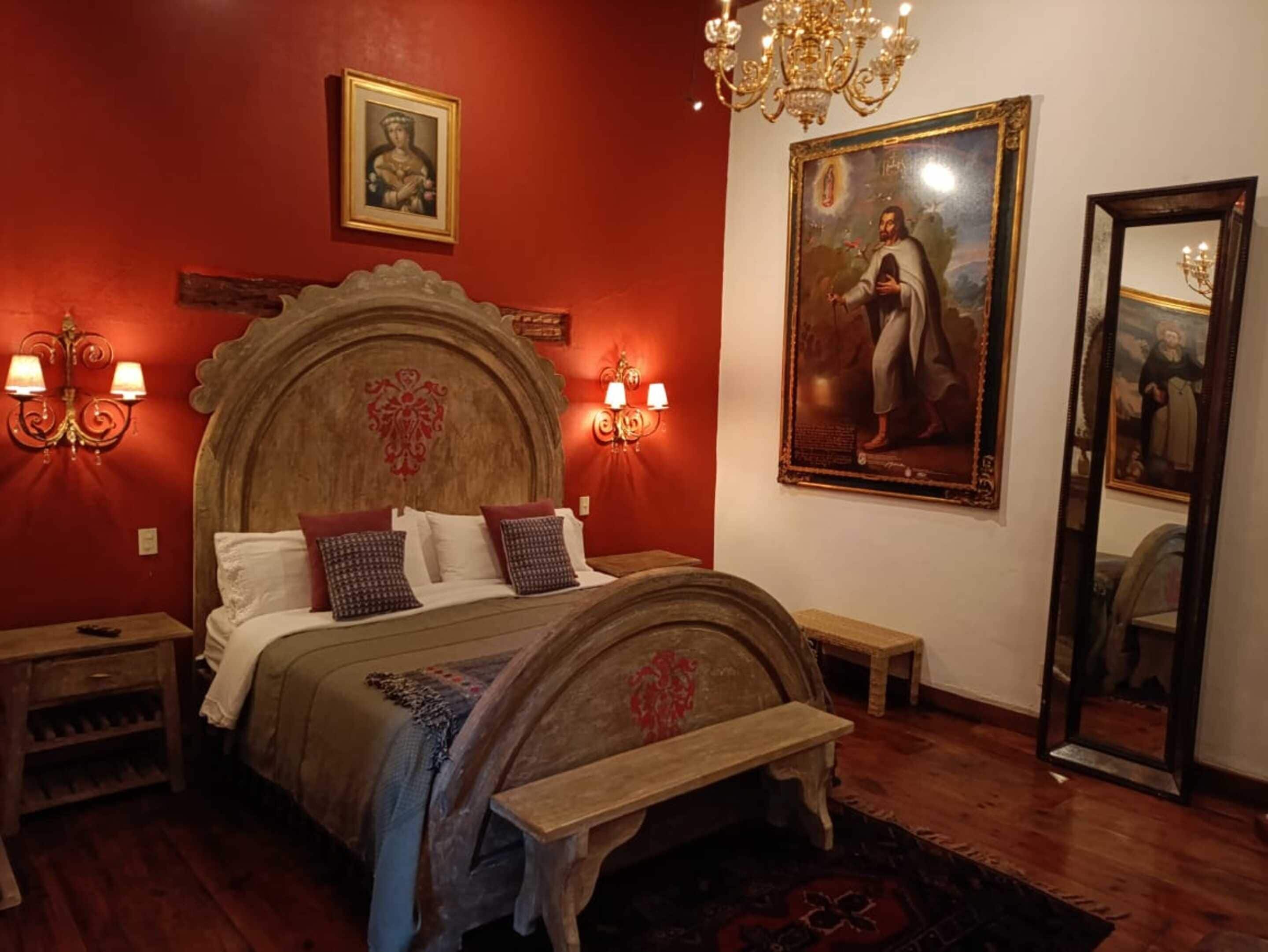 Une chambre à coucher avec un lit en bois, des murs rouges, un lustre et un grand tableau.