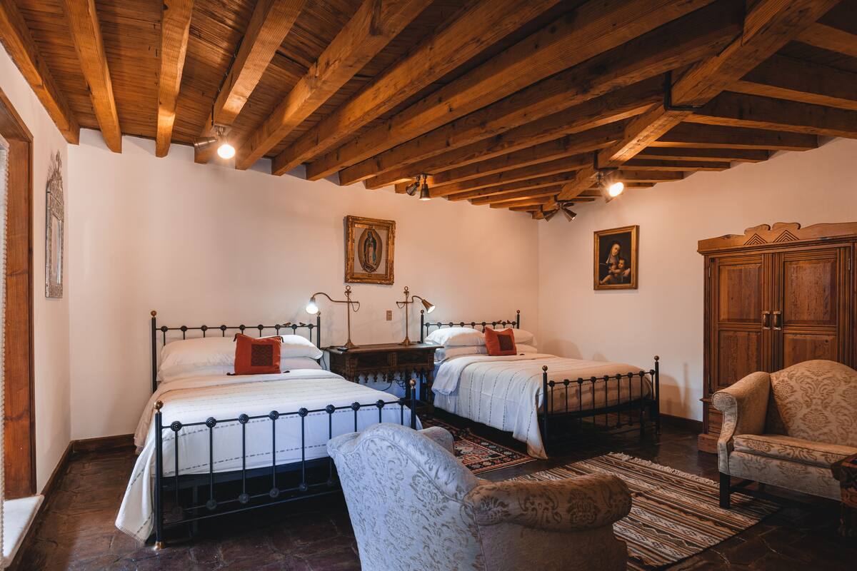 Une chambre avec deux lits, des poutres apparentes en bois au plafond, une chaise et un meuble.