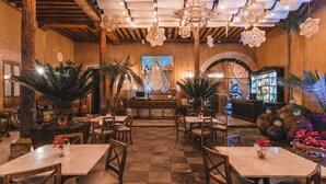 A restaurant with a bar area, wooden tables, chairs, and potted plants.