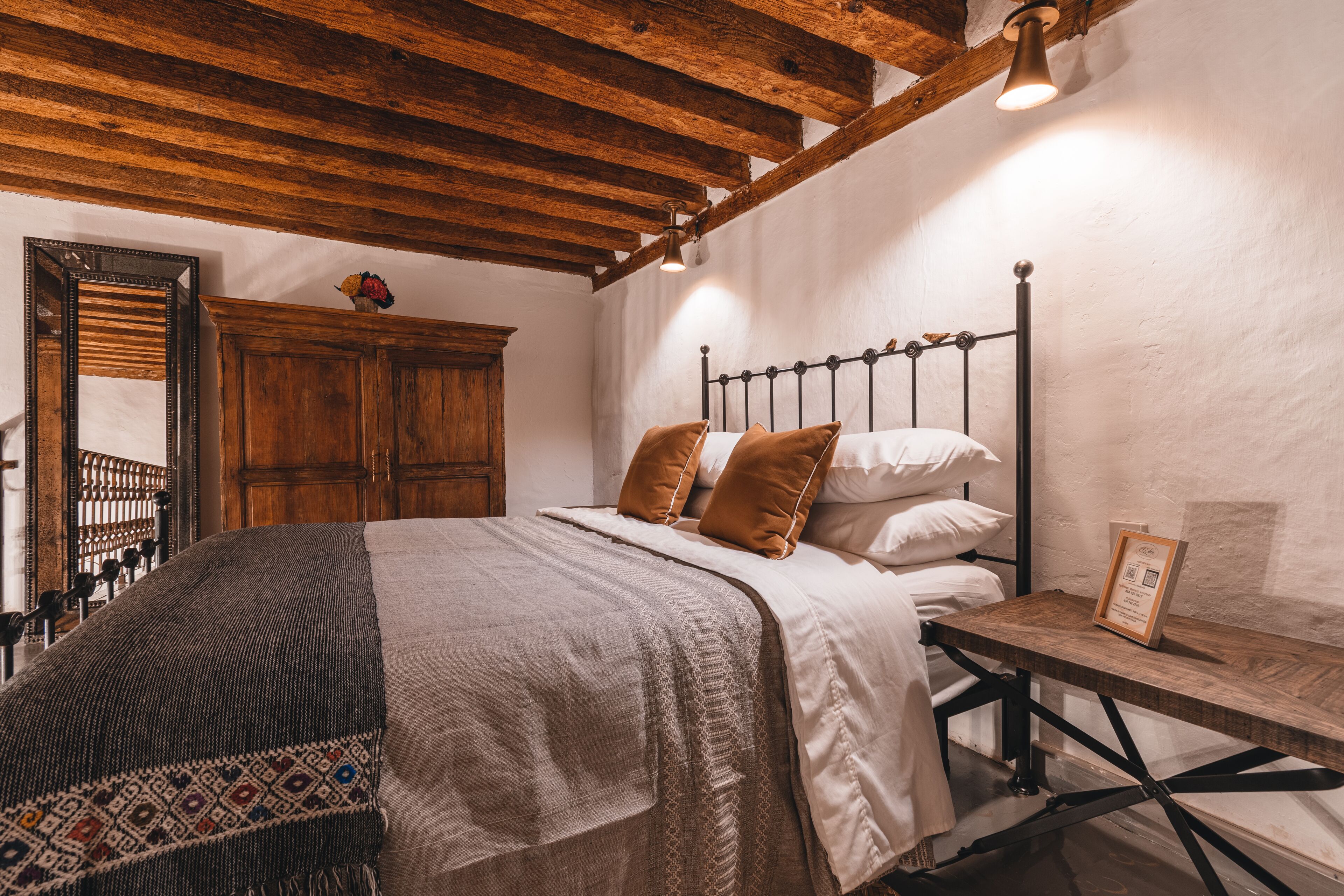 Un dormitorio con estructura de cama de madera, una mesita de noche y un espejo.