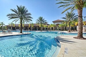 A swimming pool with clear blue water, surrounded by palm trees and a building with a tiled roof. - Fantastic Home at Solterra | SOL102 (Davenport)