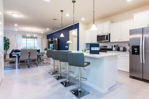 A modern kitchen with a central island, bar stools, a dining area, and a large window. - Fantastic Home at Solterra | SOL102 (Davenport)
