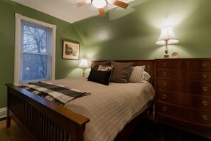 A bedroom with a bed, dresser, nightstand, lamp, and window. - Cute yellow house on Peter (Kitchener)
