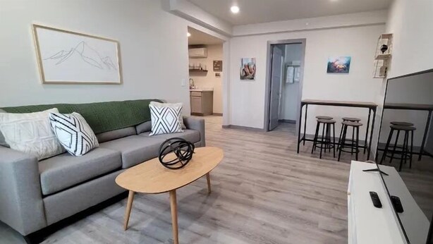 A modern living room with a grey sofa, a coffee table, a TV, and a kitchen in the background. - Elk Loft in Downtown Custer, Sleeps 8, 2 full bath (Custer)