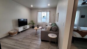 A modern living room with a flat-screen TV, a grey sofa, a small round table, and a potted plant. - Elk Loft in Downtown Custer, Sleeps 8, 2 full bath (Custer)