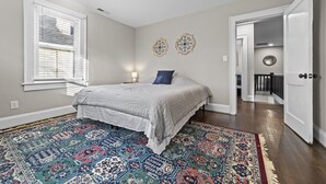 A bedroom with a large bed, a patterned rug, and two wall decorations. - Big House Downtown Greensboro (Greensboro)