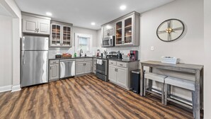 A modern kitchen with stainless steel appliances, wooden flooring, and a rustic wooden table with benches. - Big House Downtown Greensboro (Greensboro)