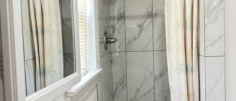 Un baño con ducha, ventana y espejo.