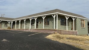 Un motel con una hilera de habitaciones, un estacionamiento techado y un área verde al frente.