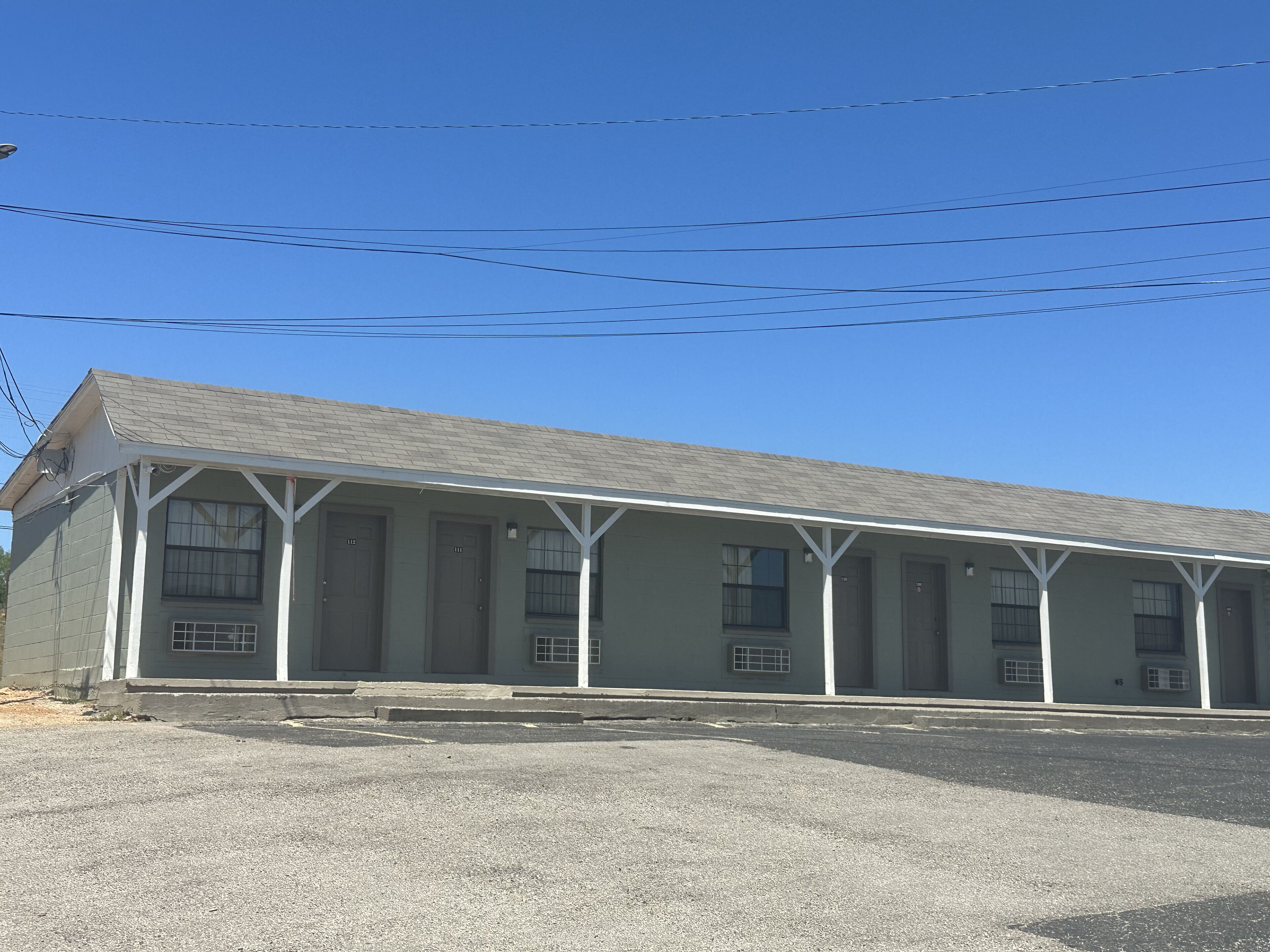 A motel with a simple, single-story structure, featuring a covered parking area and multiple rooms with individual doors.