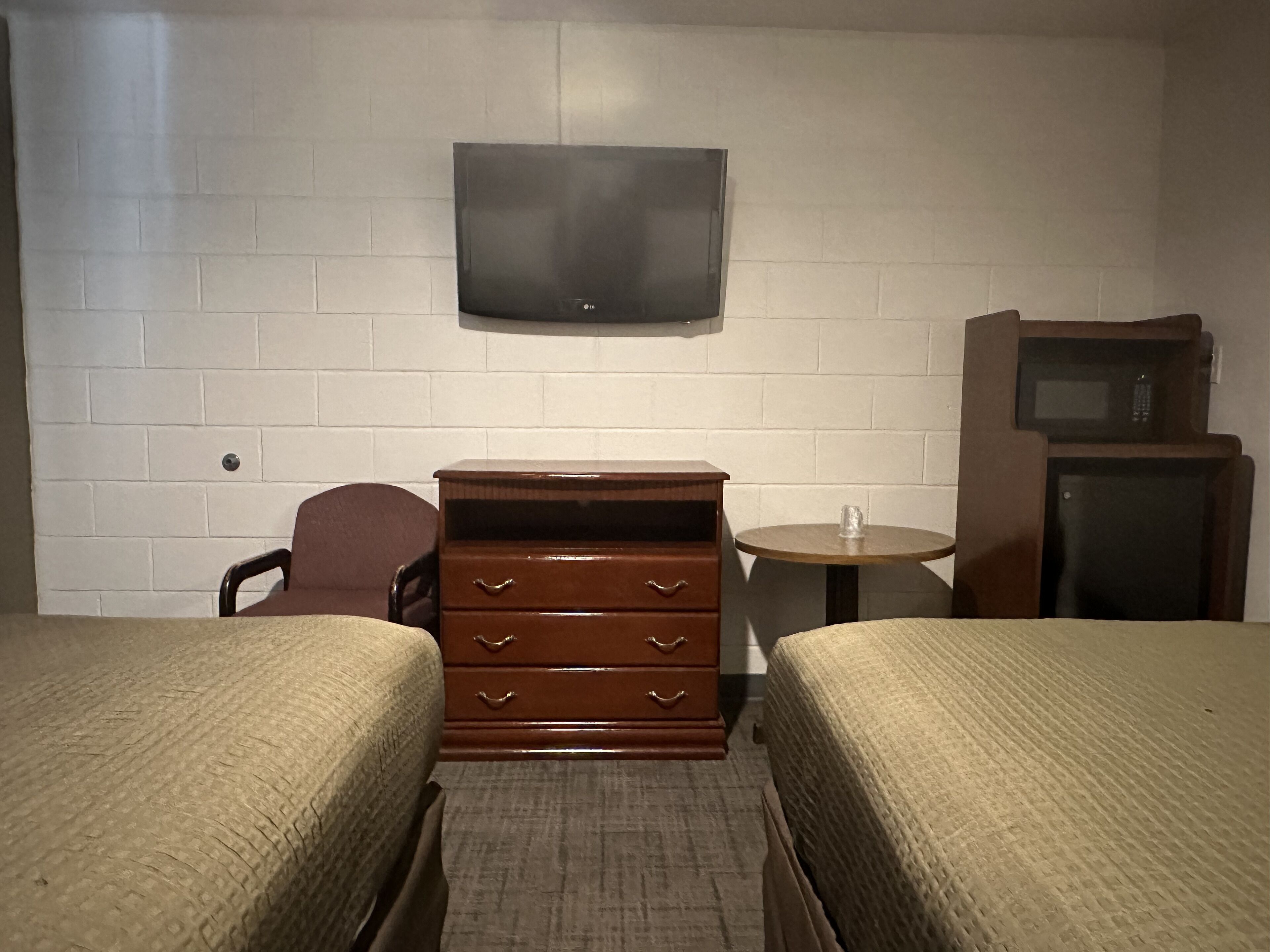 A hotel room with two beds, a wooden dresser, a television, and a microwave.