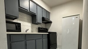 Una cocina compacta con armarios gris oscuro, un microondas negro, una estufa y un refrigerador blanco.