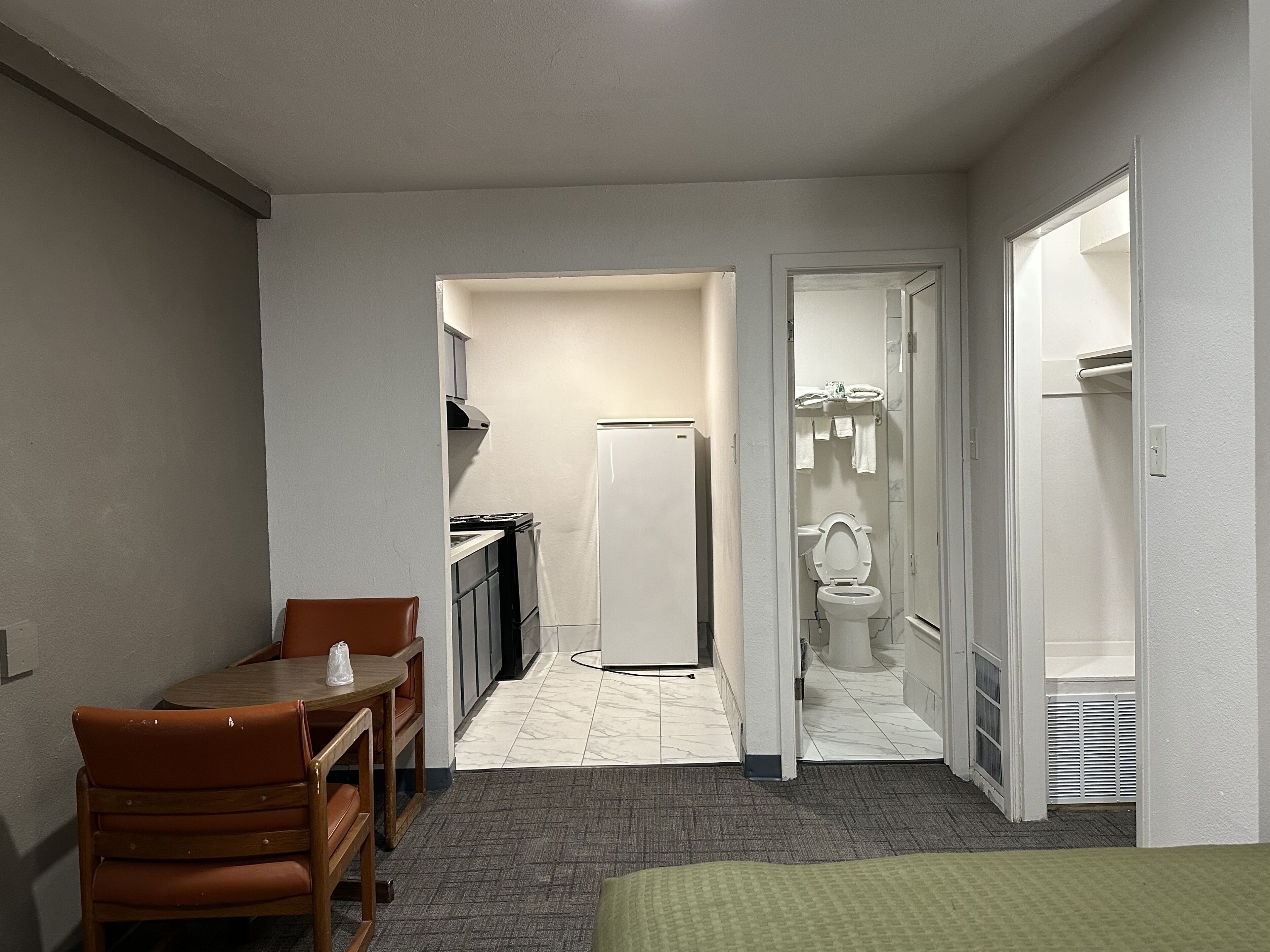 Une chambre d’hôtel compacte comprenant un coin cuisine, un espace repas avec une table et des chaises, ainsi qu’une salle de bain avec des toilettes et un lavabo.