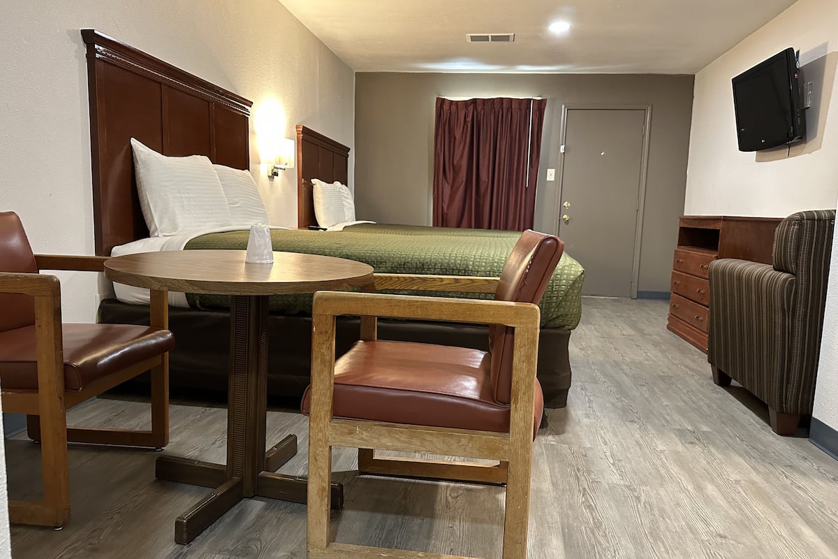 A hotel room with a bed, a desk, a chair, a dresser, and a television.