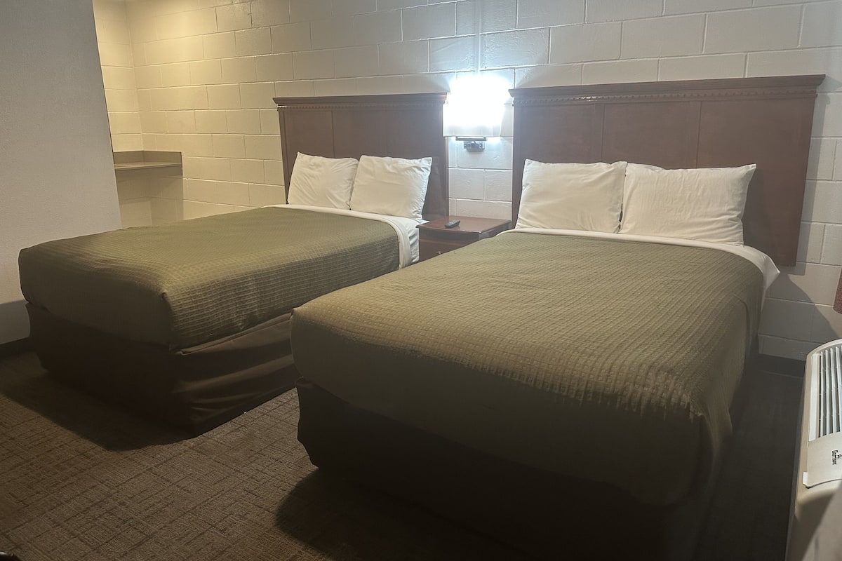 A hotel room with two single beds, a wooden headboard, a nightstand, and a small window.