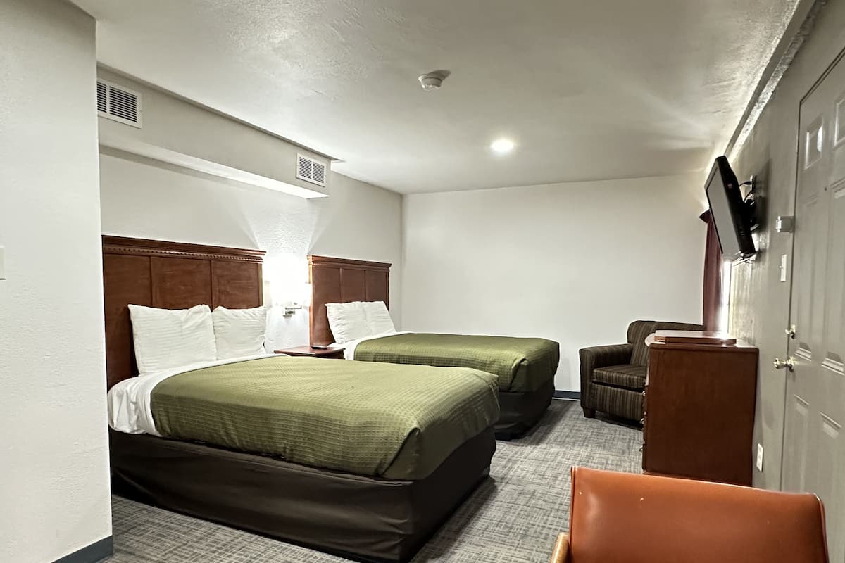 A hotel room with two beds, a desk, a chair, and a wardrobe.