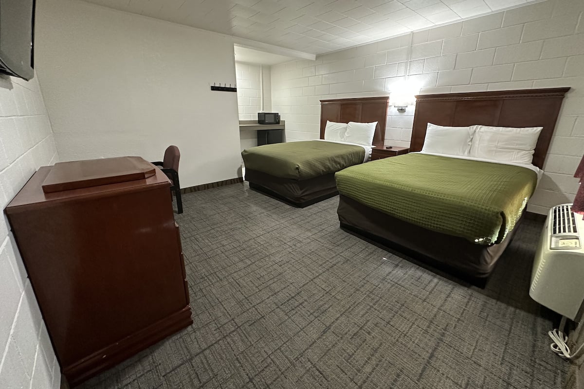 A hotel room with two beds, a desk, a chair, a microwave, and a telephone.
