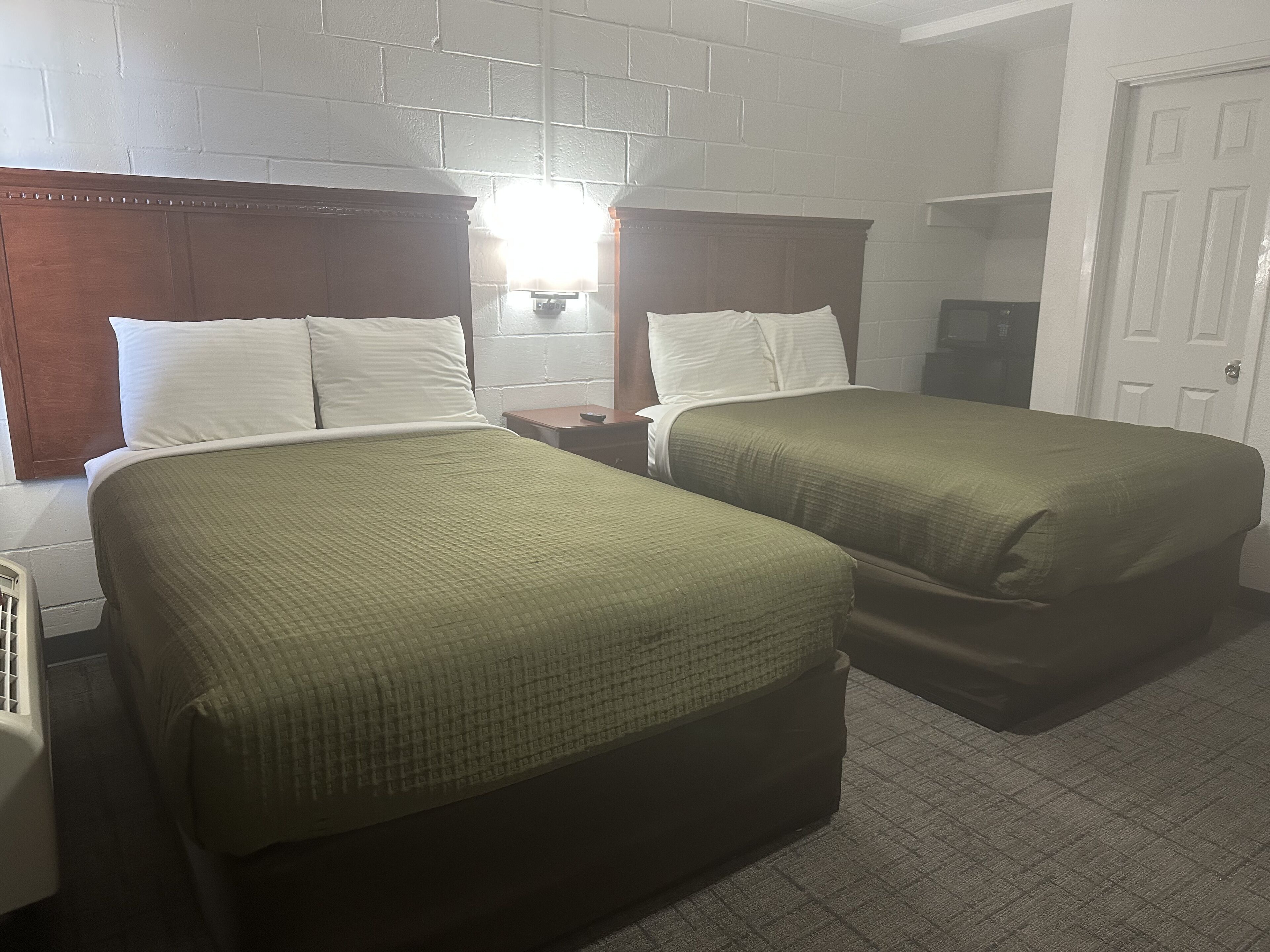 Quarto de hotel com duas camas, uma cabeceira de madeira, parede de tijolos brancos e uma porta branca.