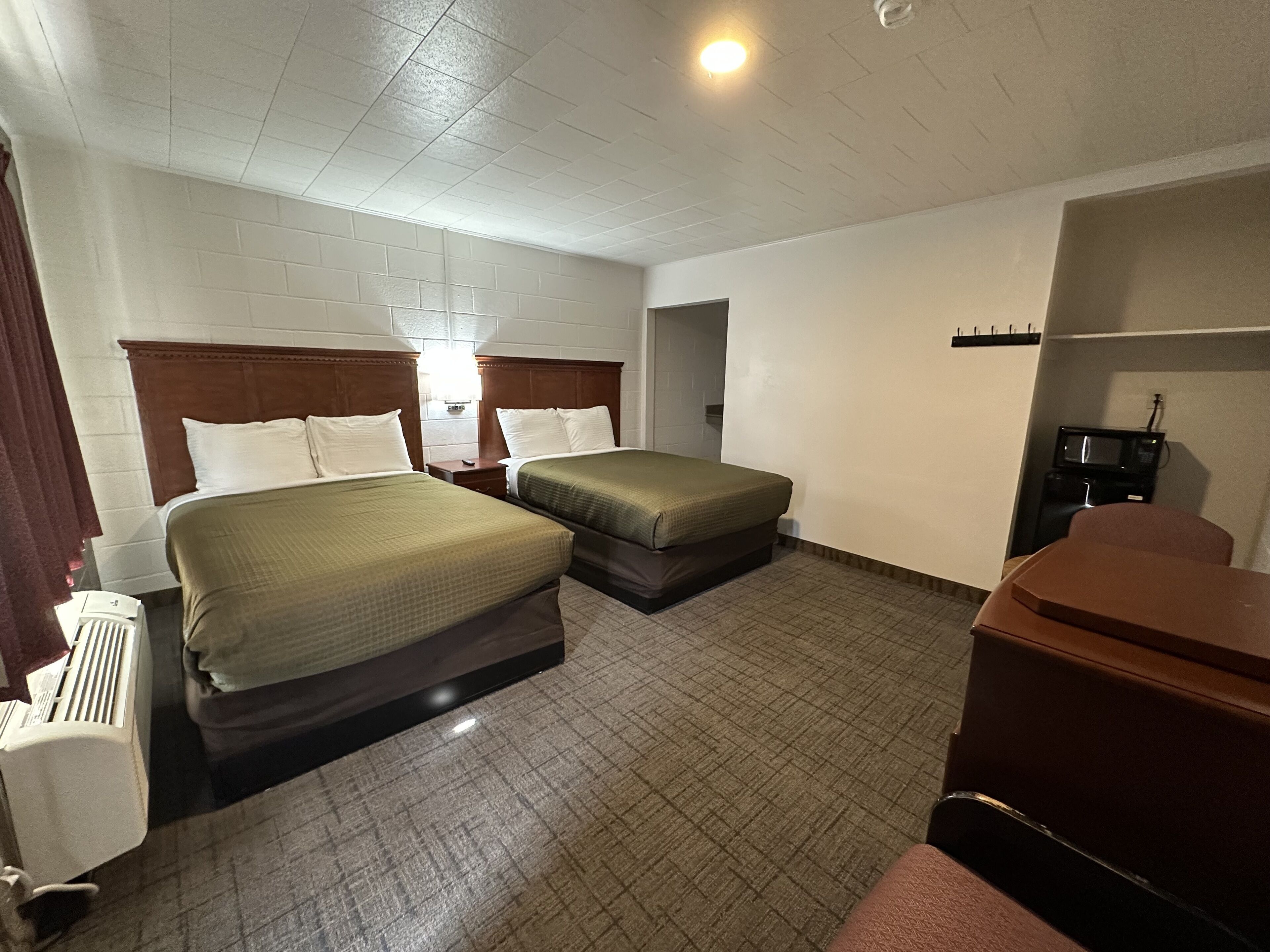 A hotel room with two beds, a desk, a chair, a microwave, and a radiator.