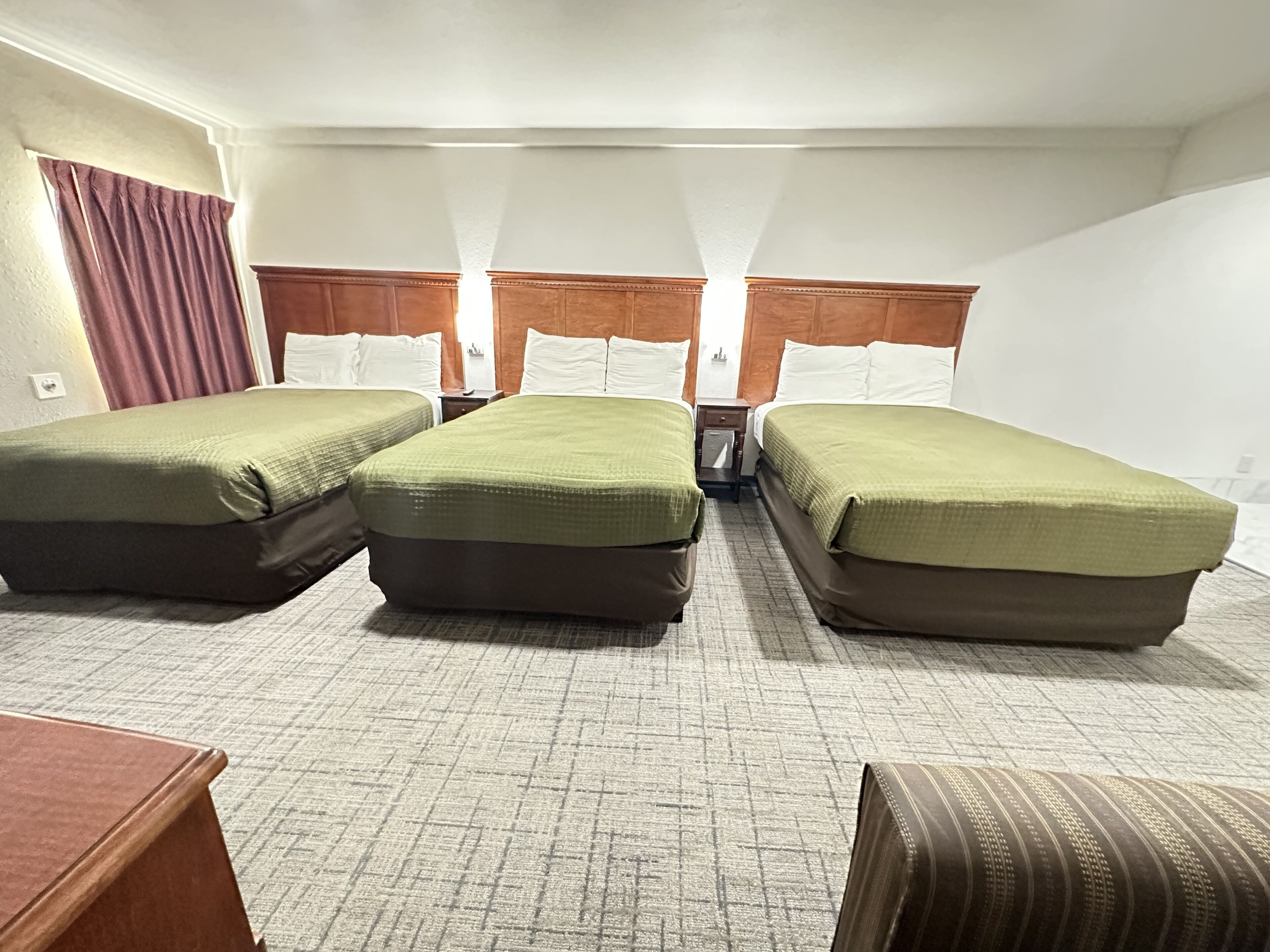 A hotel room with three single beds, a wooden headboard, a small wooden table, and a patterned carpet.