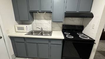 A compact kitchen with grey cabinets, a white countertop, a built-in microwave, a double sink, and a black stove with four burners.