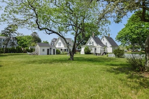 A large, white, two-story house with a spacious lawn and a large tree in the foreground.