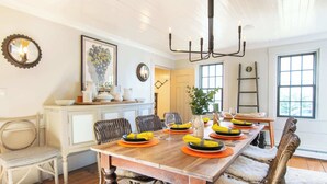 A dining room with a wooden table set for six, surrounded by wicker chairs.