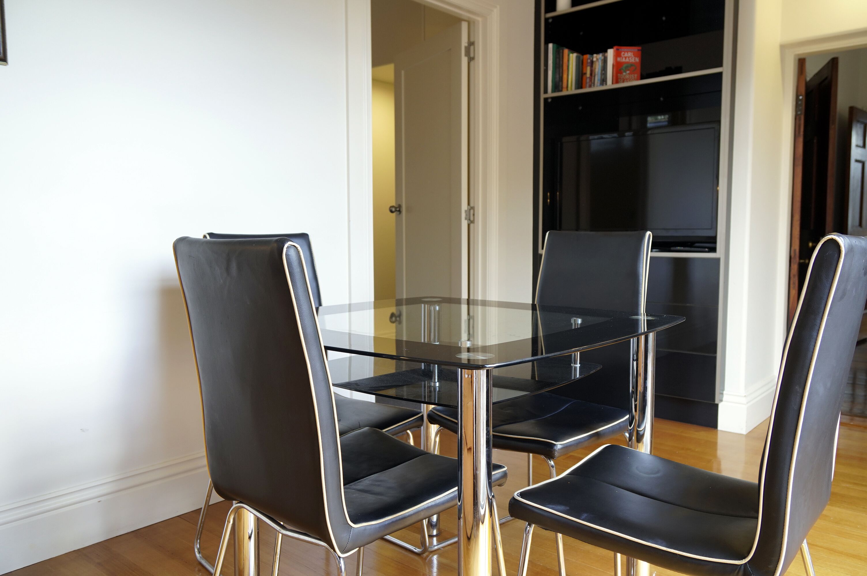 Een moderne eetruimte met een glazen tafel en vier zwarte stoelen met metalen poten.