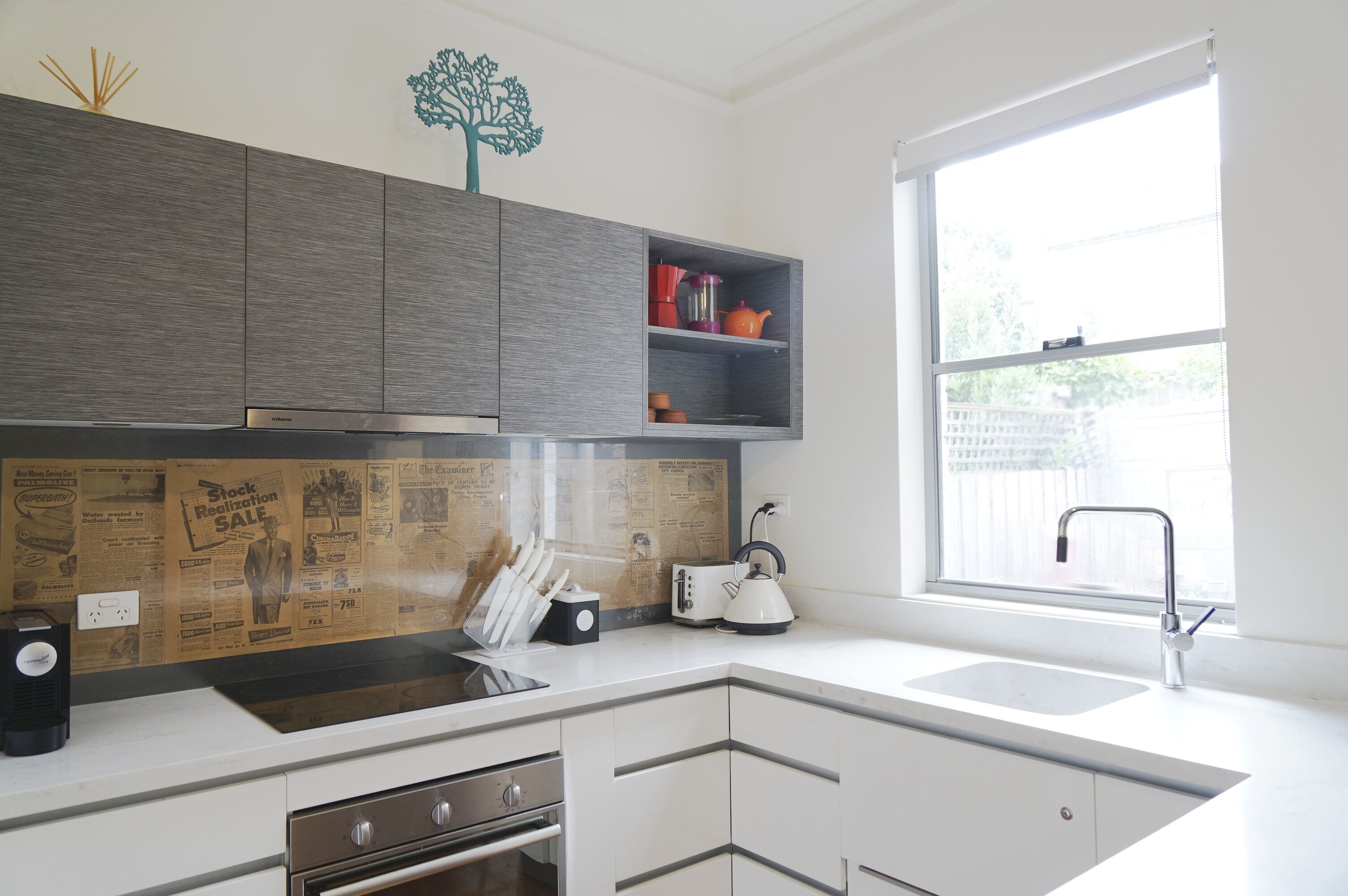 A modern kitchen with grey cabinets, a white countertop, a built-in oven, and a window with a view of the outside.