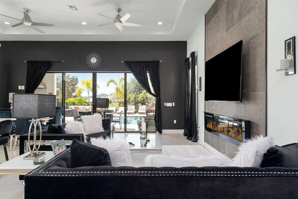 A modern living room with a black sofa, a fireplace, a flat-screen TV, and a ceiling fan.