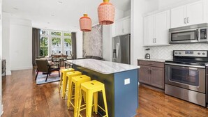 Une cuisine moderne avec des meubles blancs, des appareils en acier inoxydable et un îlot central doté de tabourets jaunes.