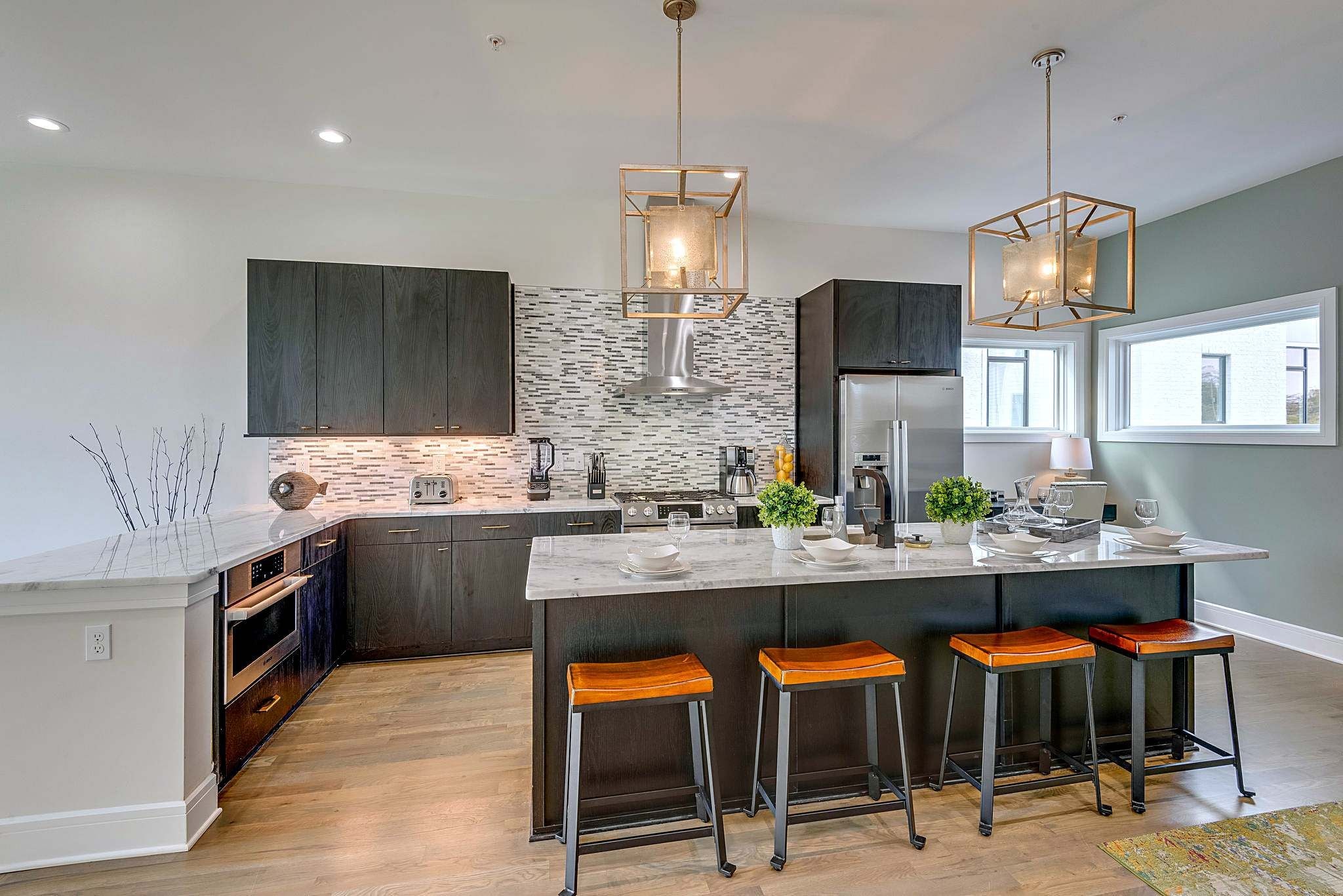 A modern kitchen with a central island, bar stools, a built-in oven, and a backsplash.
