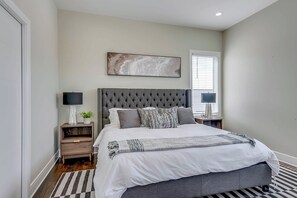 Een slaapkamer met een groot bed, nachtkastje, lamp en een raam met zonwering.