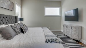 Un dormitorio con una cama grande, televisor, ventana y una alfombra estampada.