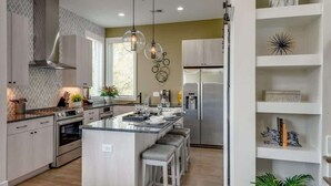 Una cocina moderna con una isla central, electrodomésticos de acero inoxidable e iluminación colgante.