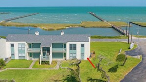 A coastal property with a two-story building, a grassy lawn, and a pier extending into the sea.