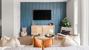 Ein modernes Wohnzimmer mit blauer Akzentwand, einem Flachbildfernseher, einem Holzschrank und einer gemütlichen Sitzecke mit Kissen.