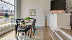 Un coin repas avec une table dressée pour quatre personnes, une grande fenêtre donnant sur des immeubles et un téléviseur à écran plat fixé au mur.