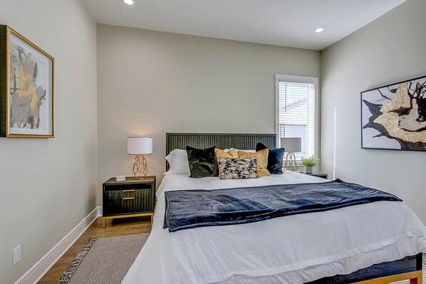 A bedroom with a bed, bedside table, lamp, and artwork.