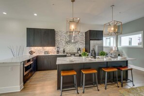 A modern kitchen with dark cabinetry, a large island with bar stools, and pendant lighting. - Walk to 12 South + Gulch | Luxury Stay w/ Parking! (Nashville)