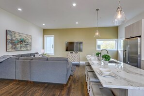 A modern kitchen with a built-in oven, a dining area with a marble countertop, and a large gray sectional sofa. - Group Getaway | Walkable Gulch Location + Parking! (Nashville)