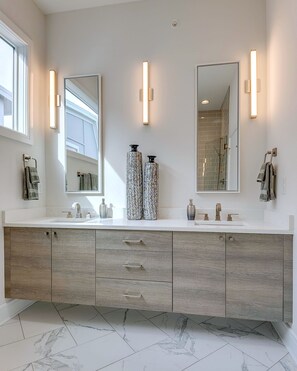 Ein modernes Badezimmer mit einem Doppelwaschbecken, zwei großen Spiegeln und beleuchteten Wandscheinwerfern.