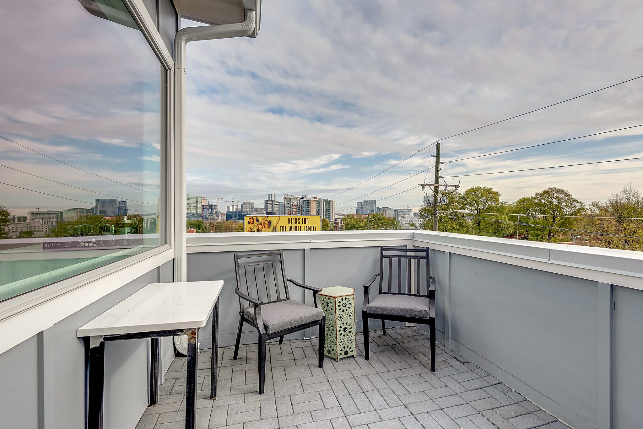 Ein Balkon mit Tisch und zwei Stühlen, Blick auf die Stadt und ein gelbes Schild.