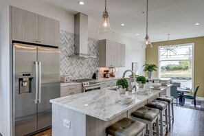A modern kitchen with a large island, stainless steel appliances, and pendant lighting. - Group Getaway | Walkable Gulch Location + Parking! (Nashville)