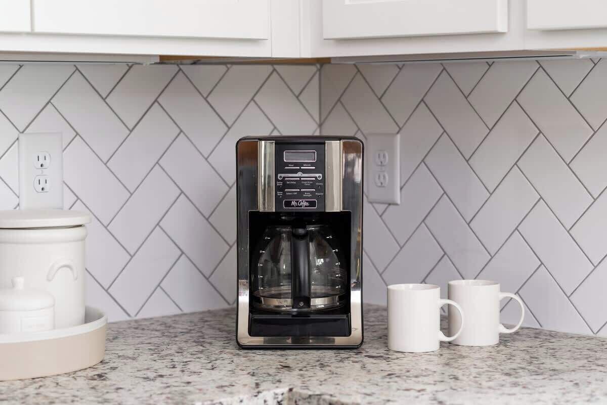 A coffee maker on a kitchen counter with a herringbone tile backsplash.