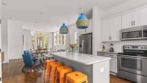 Une cuisine moderne avec des meubles blancs, des appareils en acier inoxydable et un îlot central doté de tabourets de bar.