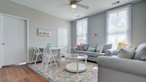 Un salon avec un canapé gris, une table basse ronde, une table à manger blanche avec des chaises et un tapis coloré.