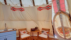 A tent with a kitchen area, two wooden chairs, a small table, and a rug.
